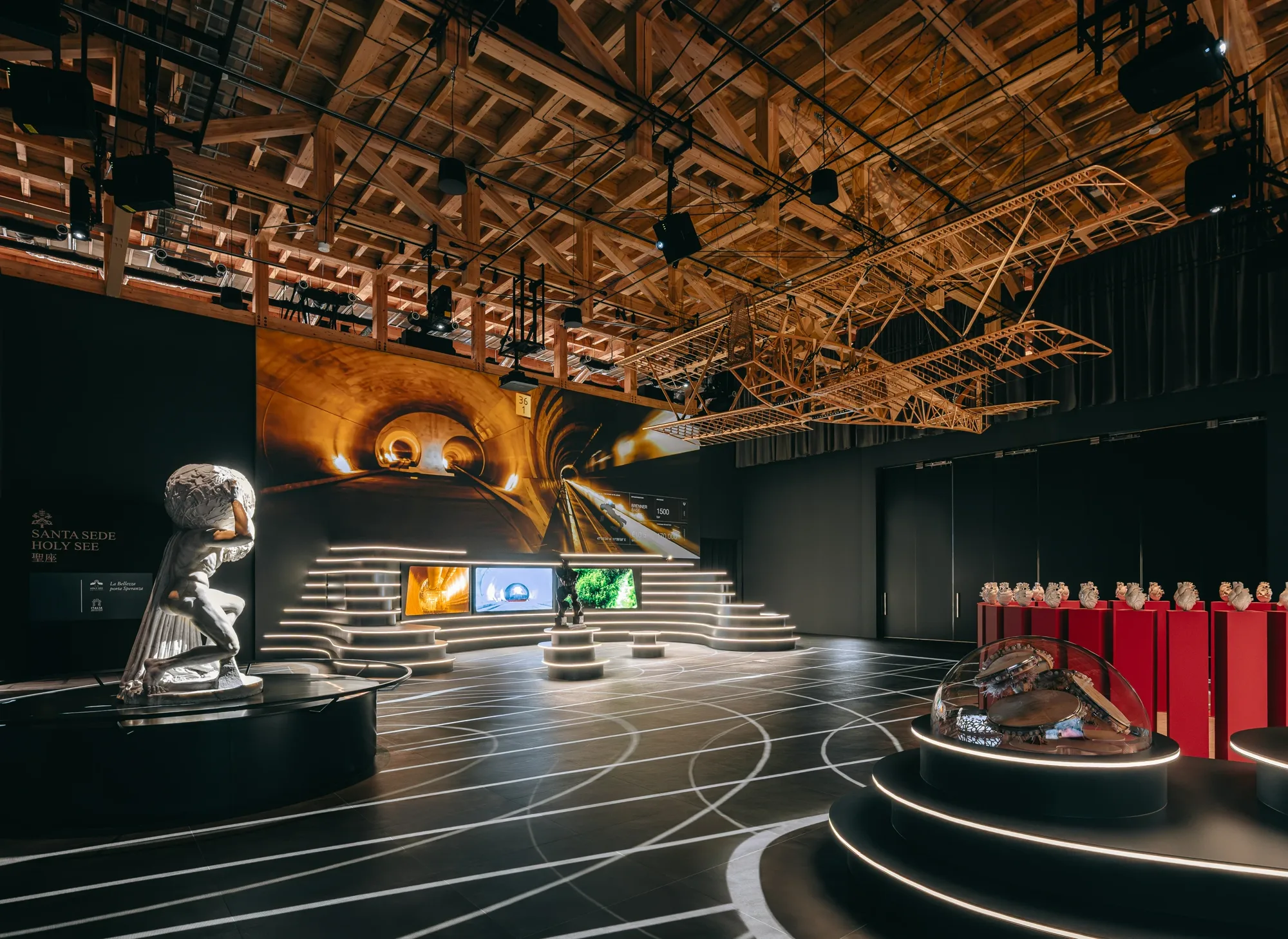 L'interno del Padiglione Italia a Expo 2025 Osaka, allestimento Exibiz con la statua di Atlante, i gradoni luminosi e le capriate in legno